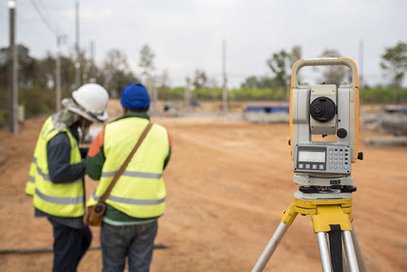 Surveyor equipment tacheometer or theodolite outdoors at construction site and construction worker in safety uniform
